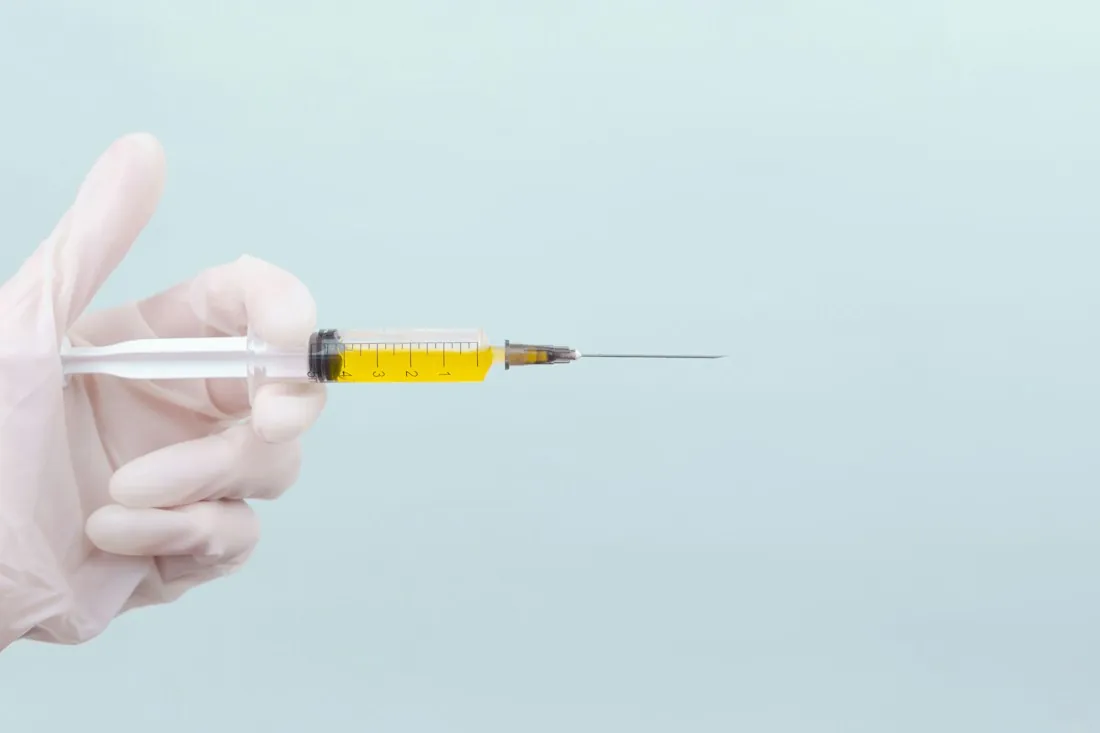 Gloved hand holding a vitamin injection syringe